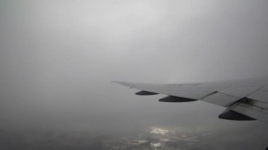 4K, kalkış sırasında uçak penceresinden görülen beyaz fırtına bulutları. Hava yoluyla seyahat etmek. Yağmurlu, gri bir günde, uçağın kanadındaki kamarada gezgin görüntüsü.