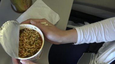 4K Asyalı kadın yolcu hazır erişte yiyor ve uçuş sırasında uçağın içinde çay içiyor.