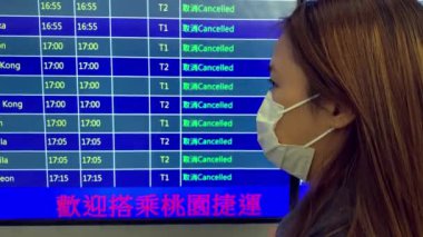 Taipei, Tayvan-15 Mart 2020: 4 K, kadın koruyucu maske takıyor ve iptal edilmiş uçaklarla havaalanı tahtasına bakıyor. Koronavirüs salgını yüzünden tüm uçuşlar iptal edildi. Covid-19-Dan