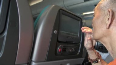 4k iç uçak, uçakta yaşlı bir Asyalı yolcu, ekran monitörünü lisen olarak kullanıyor ve kendi eğlencesi için uçuş televizyonunda bir film izliyor ve zamanın tadını çıkarıyor.