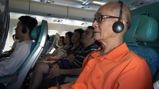 4K室内飛行機 老人アジアの旅客機彼のエンターテイメントのための飛行のモニターで映画を見て 時間フライダンを楽しむためにイヤフォンを使用して飛行機の中で — ストック動画