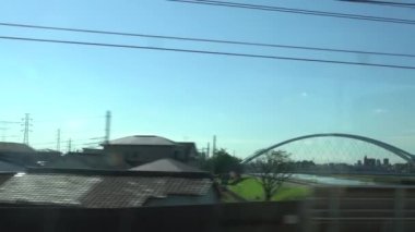 Japonya 'da güzel bir günde Tokyo' da tren yolculuğunun penceresinden 4K manzarası. Tren bir tren istasyonundan kalkıyor, Dan nehrinin üzerinden geçiyor.