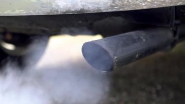 Arabanın egzoz borusundan çıkan yakın çekim dumanı beyaz dumana neden oluyor. Yoldaki araçtan zehirli karbon monoksit, hava kirliliği konsepti. Trafikte duman emisyonları