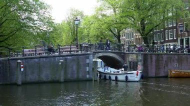Amsterdam, Hollanda-13 Mayıs 2019: 4K, şehir evleri ve tekne Amsterdam kanalı üzerindeki köprüden geçiyor. Ünlü Hollanda kanalları ve eski Avrupa şehri. Seyahat konsepti arka planda.