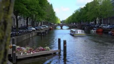 Amsterdam, Hollanda-13 Mayıs 2019: 4K, şehir evleri ve tekne Amsterdam kanalı üzerindeki köprüden geçiyor. Ünlü Hollanda kanalları ve eski Avrupa şehri. Seyahat konsepti arka planda.