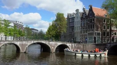Amsterdam, Hollanda-13 Mayıs 2019: 4K, kasaba evleri ve tekne kanaldaki köprüden geçiyor. Eski sokak manzarasındaki liman kanallarının yanındaki gemiler. Tekneler, Dan Nehri 'nde bir ulaşım biçimidir.