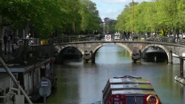 Amsterdam, Hollanda-13 Mayıs 2019: Kasaba evleri ve tekne kanaldaki köprüden geçiyor. Eski sokak manzarasındaki liman kanallarının yanındaki gemiler. Tekneler, Dan Nehri 'nde bir ulaşım biçimidir.