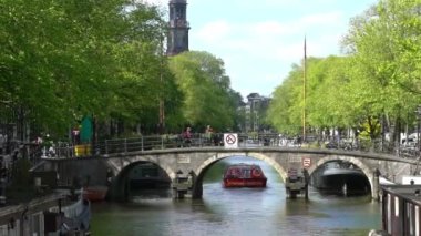 Amsterdam, Hollanda-13 Mayıs 2019: Kasaba evleri ve tekne Amsterdam kanalı üzerindeki köprüden geçiyor. Ünlü Hollanda kanalları ve eski Avrupa şehri. Seyahat konsepti arka planda.