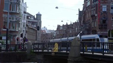 Amsterdam, Hollanda-13 Mayıs 2019: 4k, Tramvaylar ve turistler caddeyi geçiyor. Tramvay Hollanda 'daki eski kasabanın merkez bölgesinden geçiyor. Apartman binaları var. Toplu taşıma kavramı.