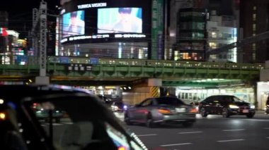 Tokyo, Japonya-31 Ocak 2020: 4K, yüksek tren şehrin üzerinden geçerken yolda giden trafik araçları. Japon arabası geceleyin kasaba caddesinden geçer. Toplu taşıma kavramı Metropolitan-Dan