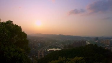 Taipei şehrinin gün batımında ormandaki trafik arabalarıyla 4K hava görüntüsü. Şehir manzarasında güneş ışığı gören güzel bir çevre yolu manzarası. Güzellik Dağı Xindian - Dan