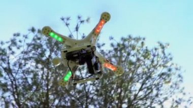 4K, RC İHA uçuşu. Ağaçların arka planında. Yüksek teknoloji yenilikleri. Uzaktan kumandalı modern bir dronu oynayan profesyonel bir oyuncu. Kameralı kırmızı ve yeşil kuadrokopter.