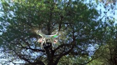 4K, RC İHA uçuşu. Ağaçların arka planında. Yüksek teknoloji yenilikleri. Uzaktan kumandalı modern bir dronu oynayan profesyonel bir oyuncu. Kameralı kırmızı ve yeşil kuadrokopter.