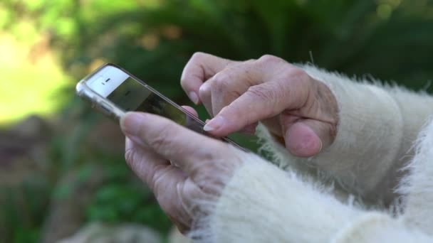 4K祖母の古い手は携帯電話を保持します おばあちゃんが使って庭の家でスマートフォンを見て — ストック動画