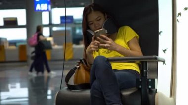 4K, uluslararası havaalanında cep telefonunda yazan genç Asyalı kadın. Kız akıllı telefonu kontrol edip internette sörf yapıyor. Bekleme odasında oturan insanlar seyahat etmek için uçağa biniyorlar.