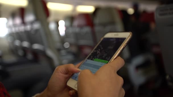飛行機の中で携帯電話を持つ4Kの若い女性 飛行機の中でスマートフォンを使っているアジアの女の子 フライト中にデバイス電話を使用している乗客 旅行者チェック スマートフォン Dan — ストック動画
