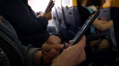 4K, uçağın içinde cep telefonu olan beyaz bir kadın. Uçakta akıllı telefonu tutan bir kadın el. Uçuş sırasında cihaz telefonu kullanan bir yolcu. İnsanlar akıllı telefonları kontrol eder.