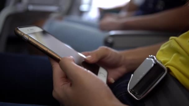 飛行機の中で携帯電話を持つ4Kの若い女性 飛行機の中でスマートフォンを使っているアジアの女の子 フライト中にデバイス電話を使用している乗客 旅行者チェック スマートフォン Dan — ストック動画
