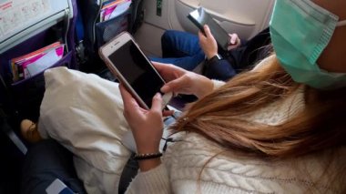 4K, Asya 'lı kadın akıllı telefonu tutuyor ve uçuş sırasında bulaşan 2019-NCoV enfeksiyonuna karşı maske takıyor. Gezginler uçaktaki Coronavirüs 'ü korumak için maske kullanıyor.