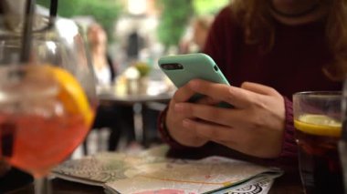 4K, beyaz kadın barda akıllı telefon kullanıyor, bir bardak aperol kokteyli. İtalyan restoranında cep telefonuna dokun. İnternette sörf yapmak, sosyal ağı kontrol etmek ve mobil Dan 'e metin yazmak