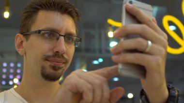 Akıllı telefon kullanan, ekranlara dokunup insanlarla iletişim kuran mutlu beyaz adamın yavaş çekimleri. İnternette sörf yapmak, sosyal ağları kontrol etmek ve telefon cihazına yapılan metinleri yazmak. Yavaş çekim 120 fps-Dan