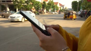 4K Asyalı kadın Siem Reap 'te trafik arabalarıyla sokakta cep telefonu kullanıyor. Kamboçya 'da akıllı telefon kullanan bir kız. Cihaz telefonu kullanan bir turist. İnsanlar akıllı telefonları kontrol eder.