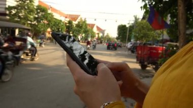 4K Asyalı kadın Siem Reap 'te trafik arabalarıyla sokakta cep telefonu kullanıyor. Kamboçya 'da akıllı telefon kullanan bir kız. Cihaz telefonu kullanan bir turist. İnsanlar akıllı telefonları kontrol eder.