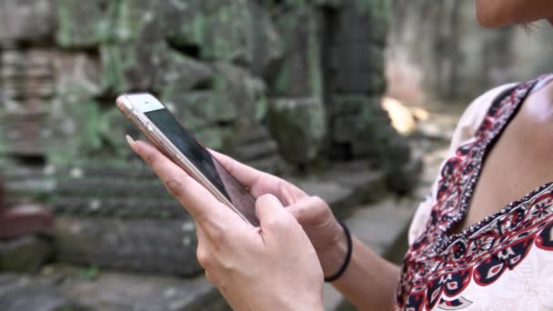 Prohm古代ヒンドゥー教寺院の有名なランドマークで携帯電話を保持し 入力する観光アジアの女性の閉鎖 女の子はスマートフォンをチェックし カンボジアの休暇でインターネットでサーフィン — ストック動画