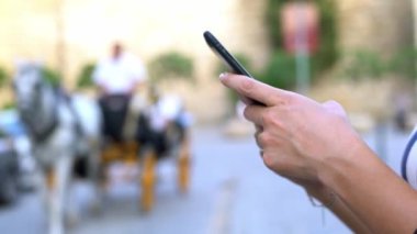 4K, Sevilla caddesinde at ve at arabaları arka plandan geçerken elinde cep telefonu olan Asyalı turist kadını kapat ve daktilo et. İspanya 'da akıllı telefonları ve sörf internetlerini kontrol et.