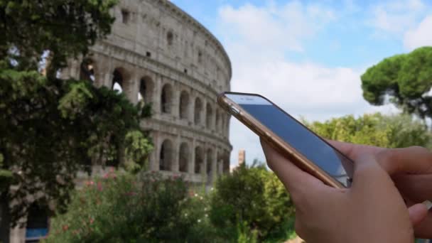 バックグラウンドでコロシアムとスマートフォン上のアジアの女性メッセージング ローマの街で携帯電話の会話をしている女の子 旅行中にデバイス電話を使用している人 — ストック動画