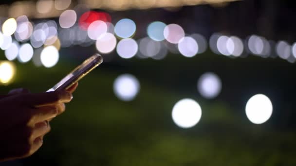 女性の手の近くに保持し 背景に光で夜にタッチスクリーンスマートフォン 台北で携帯電話を使うアジア人女性 スマートフォンで女の子のメッセージング デバイスを使う人 Mobile Dan — ストック動画
