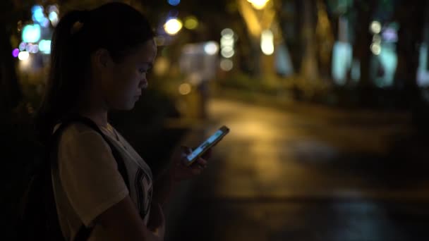 4Kアジアの女性は 台湾の路上で夜に携帯電話を使用します インターネットをサーフィンし 写真を見るためにスマートフォンを使用して 彼女の携帯電話デバイス上で行われたソーシャルネットワークをチェックします — ストック動画