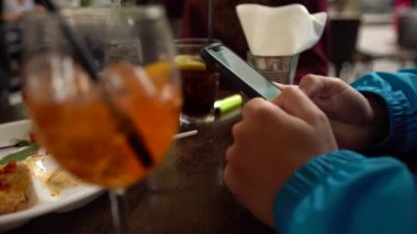 4K, beyaz adam barda akıllı telefon kullanıyor, bir bardak aperol kokteyli. İtalyan restoranında cep telefonuna dokun. İnternette sörf yapmak, sosyal ağı kontrol etmek ve mobil Dan 'e metin yazmak