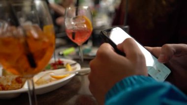 4K, beyaz adam barda akıllı telefon kullanıyor, bir bardak aperol kokteyli. İtalyan restoranında cep telefonuna dokun. İnternette sörf yapmak, sosyal ağı kontrol etmek ve mobil Dan 'e metin yazmak