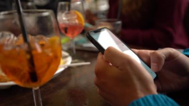 4K, beyaz adam barda akıllı telefon kullanıyor, bir bardak aperol kokteyli. İtalyan restoranında cep telefonuna dokun. İnternette sörf yapmak, sosyal ağı kontrol etmek ve mobil Dan 'e metin yazmak