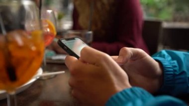 4K, beyaz adam barda akıllı telefon kullanıyor, bir bardak aperol kokteyli. İtalyan restoranında cep telefonuna dokun. İnternette sörf yapmak, sosyal ağı kontrol etmek ve mobil Dan 'e metin yazmak