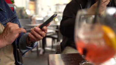 4K, beyaz kadın barda akıllı telefon kullanıyor, bir bardak aperol kokteyli. İtalyan restoranında cep telefonuna dokun. İnternette sörf yapmak, sosyal ağı kontrol etmek ve mobil Dan 'e metin yazmak