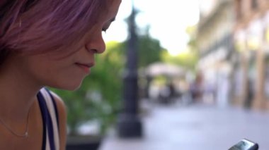 4K, Asyalı kadın Sevilla 'nın şehir caddesinde akıllı telefondan mesaj atıyor. İspanya 'da cep telefonu sohbeti yapan bir kız. Seyahat sırasında gezginler cihaz telefonu kullanıyor