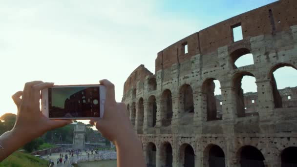 4Kローマ市内の有名なランドマークである美しいコロシアムの写真を撮るためにスマートフォンを使用して観光客の女性のクローズアップ イタリアの休暇でカメラ電話で写真を撮る人 バックパッキング旅行 — ストック動画