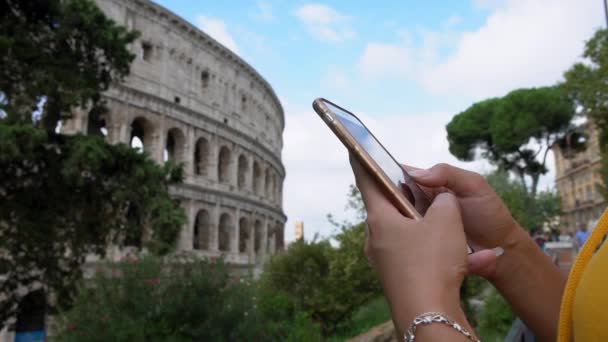 クローズアップ女性の手を保持し コロシアムの背景を持つタッチスクリーンスマートフォン 携帯電話を使うアジア人女性 スマートフォンで女の子のメッセージング 旅行中にデバイスモバイルを使用している旅行者 — ストック動画