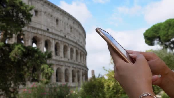 ローマの有名なランドマークのコロシアムで携帯電話を保持し 入力する観光アジアの女性の閉鎖 女の子はイタリアの休暇でスマートフォンをチェックし インターネットでサーフィン — ストック動画