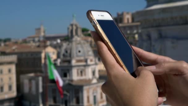 バックグラウンドでイタリアのフラグでスマートフォン上のアジアの女性メッセージング ローマの街で携帯電話の会話をしている女の子 旅行中にデバイス電話を使用している人 — ストック動画