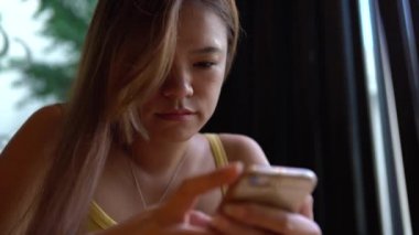 Kahvehanede akıllı telefon kullanan 4K Asyalı kadın. Sohbet etmek ve insanlarla iletişim kurmak için ekrana dokun. İnternette sörf yapmak için iyi bir zaman, sosyal ağları kontrol etmek ve onun telefon cihazına yapılan metinleri yazmak için.