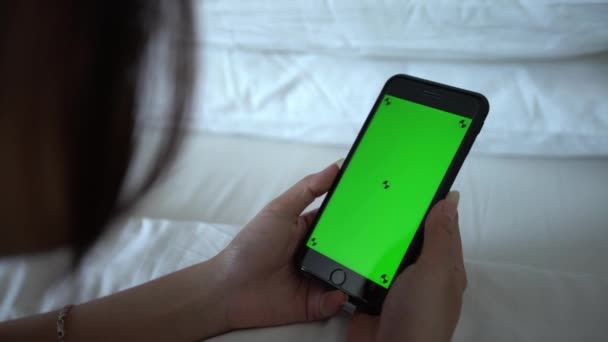 美丽的亚洲女人躺在床上 在一间有白色床单的酒店房间里展示绿色荧幕电话 用智能手机做广告 女孩手持装置电话 Dan — 图库视频影像