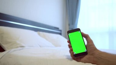 4K, Kafkasyalı bir adam otel odasında beyaz çarşaflı yeşil ekranlı bir telefon gösteriyor, bir reklam için Smartphone kullanıyor.