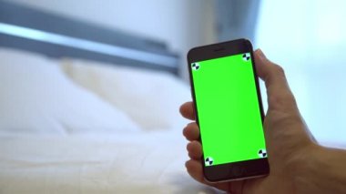 4K, Kafkasyalı bir adam otel odasında beyaz çarşaflı yeşil ekranlı bir telefon gösteriyor, bir reklam için Smartphone kullanıyor.