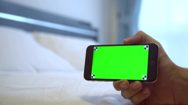 白人男子展示了一个绿色屏幕手机 在酒店房间里有一张白色床单 用智能手机做一个广告 — 图库视频影像