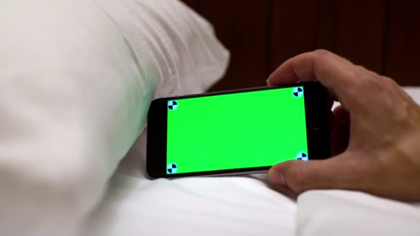 白人男性は 1つの広告のためのスマートフォンを使用して ホテルの部屋に白いシート付きのベッドと緑の画面の電話を示していますダン — ストック動画