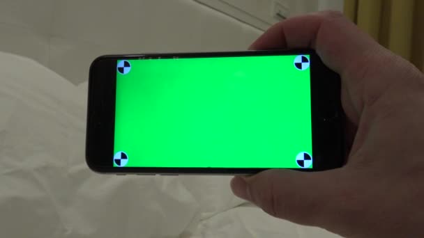 白人男子展示了一个绿色屏幕手机 在酒店房间里有一张白色床单 用智能手机做一个广告 — 图库视频影像