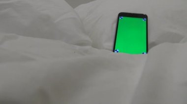 4K, yeşil ekranlı telefon çift kişilik yatakta beyaz çarşaflı bir otel odasında.